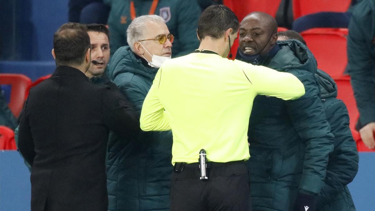 El colegiado Ovidiu Hategan frente a los técnicos del Basaksehir turco, que protestan y fuerzan la salida del campo en el partido de Champions ante el PSG.