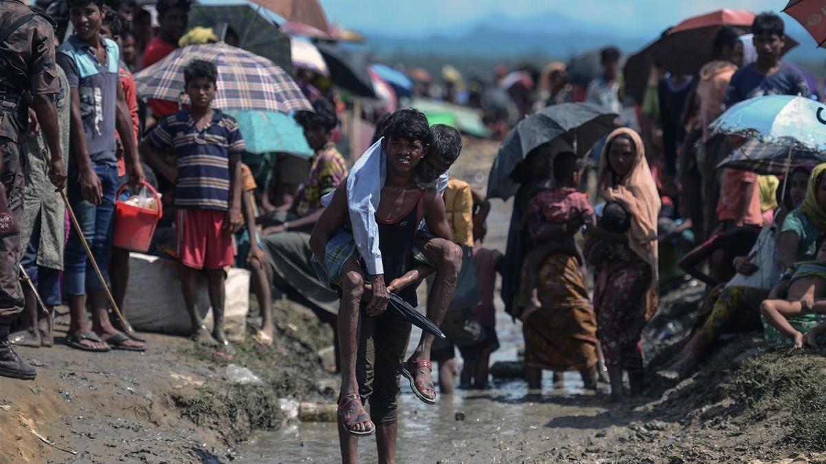 Un joven refugiado rohingya lleva a cuestas un hombre mayor en una zona cercana al lado bangladesí de la frontera con Birmania, tras cruzar el río Naf, el 17 de octubre.