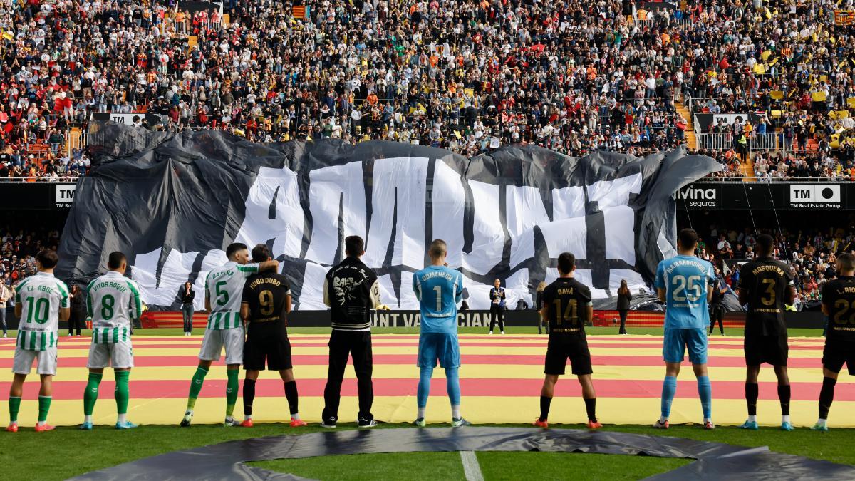 Los jugadores del Valencia y del Real Betis observan el despliegue de una pancarta en Mestalla