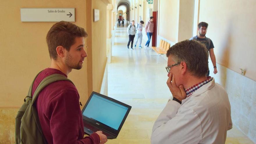 Un alumno consulta a un profesor sobre una práctica en los pasillos de la Universidad.