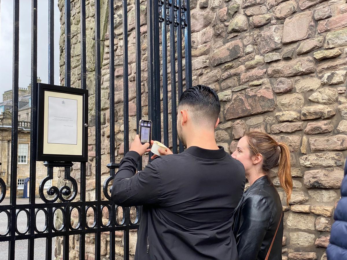 Una pareja fotografía el comunicado sobre la muerte de Isabel II colgado a las puertas del palacio de Holyrood, este viernes en Edimburgo.