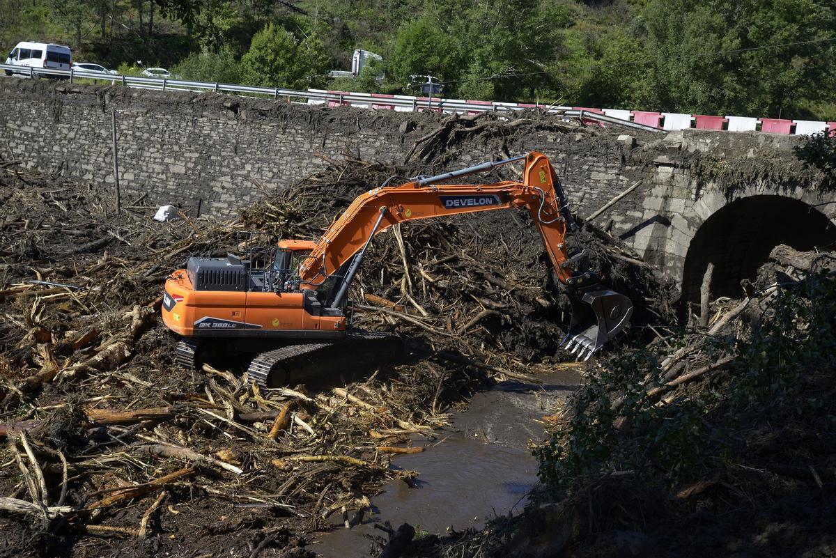 Una excavadora retira material acumulado contra el puente, que sirvió de escudor protector del pueblo de Pradocabalos.