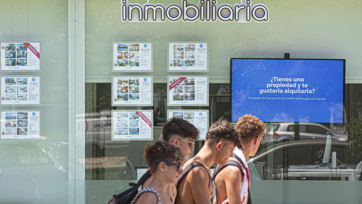 Un grupo de jóvenes pasa delante del escaparate de una inmobiliaria.