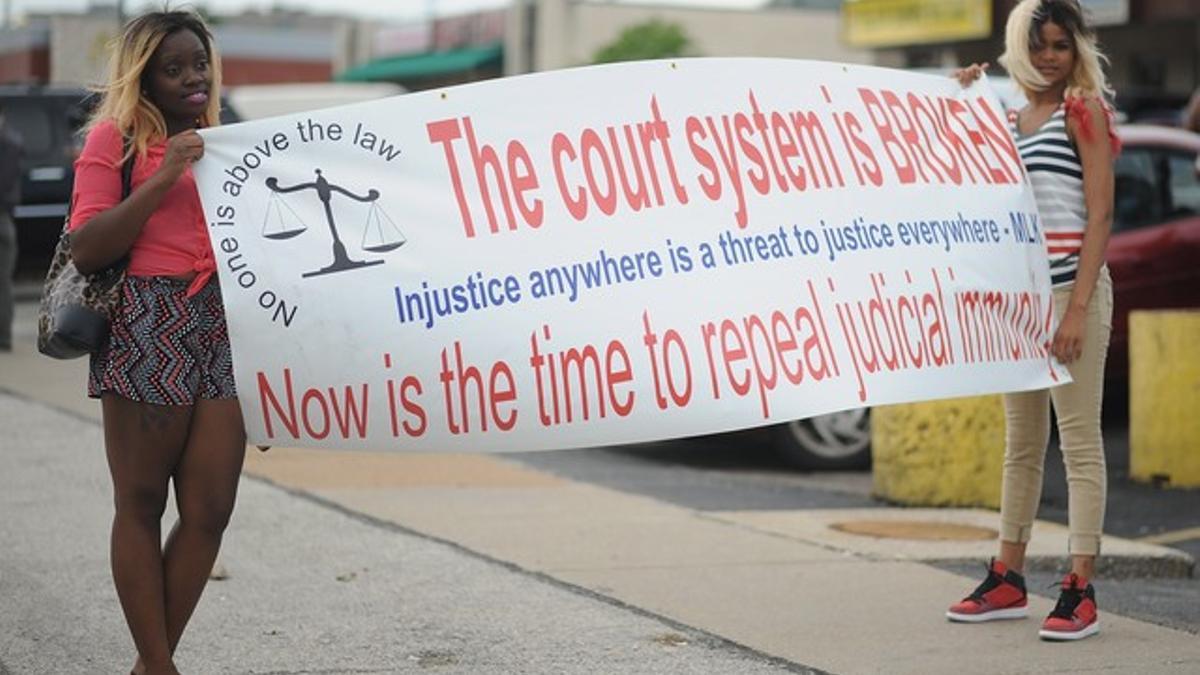 Dos jóvenes protestan en Ferguson con una pancarta contra el sistema judicial estadounidense.