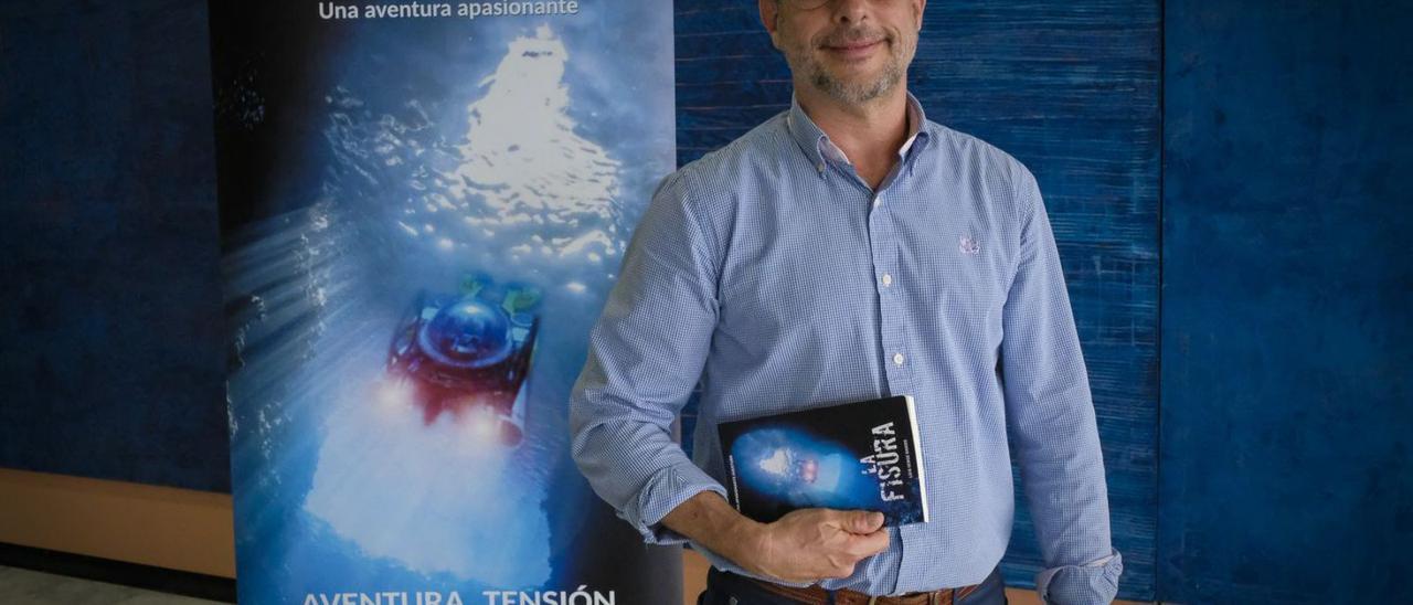 Luis Verge con un ejemplar de su libro ‘La fisura’ y ante el cartel promocional de la novela.