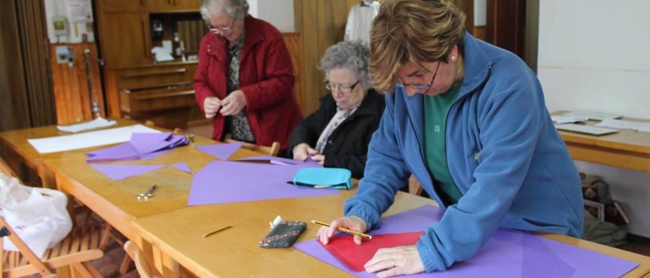 Por la izquierda, Rosi Menéndez, Marisa Suárez e Isabel Riancho, preparando banderines en el salón parroquial de Lugones.