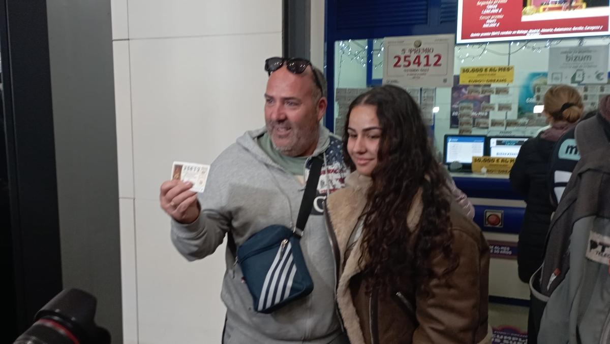 Un turista de Canarias, junto a su hija, muestran su décimo premiado en el Vialia