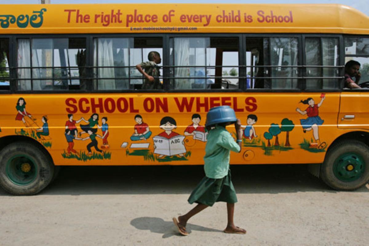 Una nena es cobreix el cap amb un recipient de plàstic mentre passa per davant d’un autobús escolar en la ciutat índia de Haidarabad.