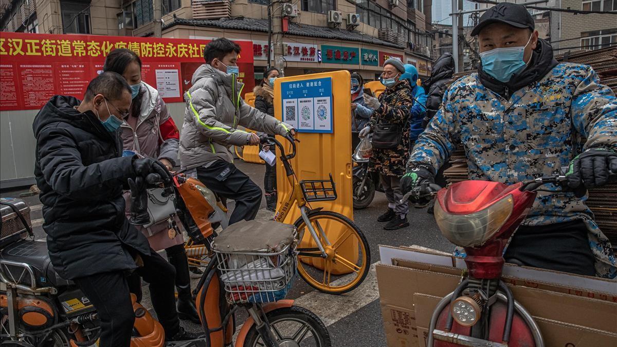 Ciudadanos de Wuhan pasan ante un punto de control donde voluntarios comprueban sus códigos sanitarios para prevenir contagios.