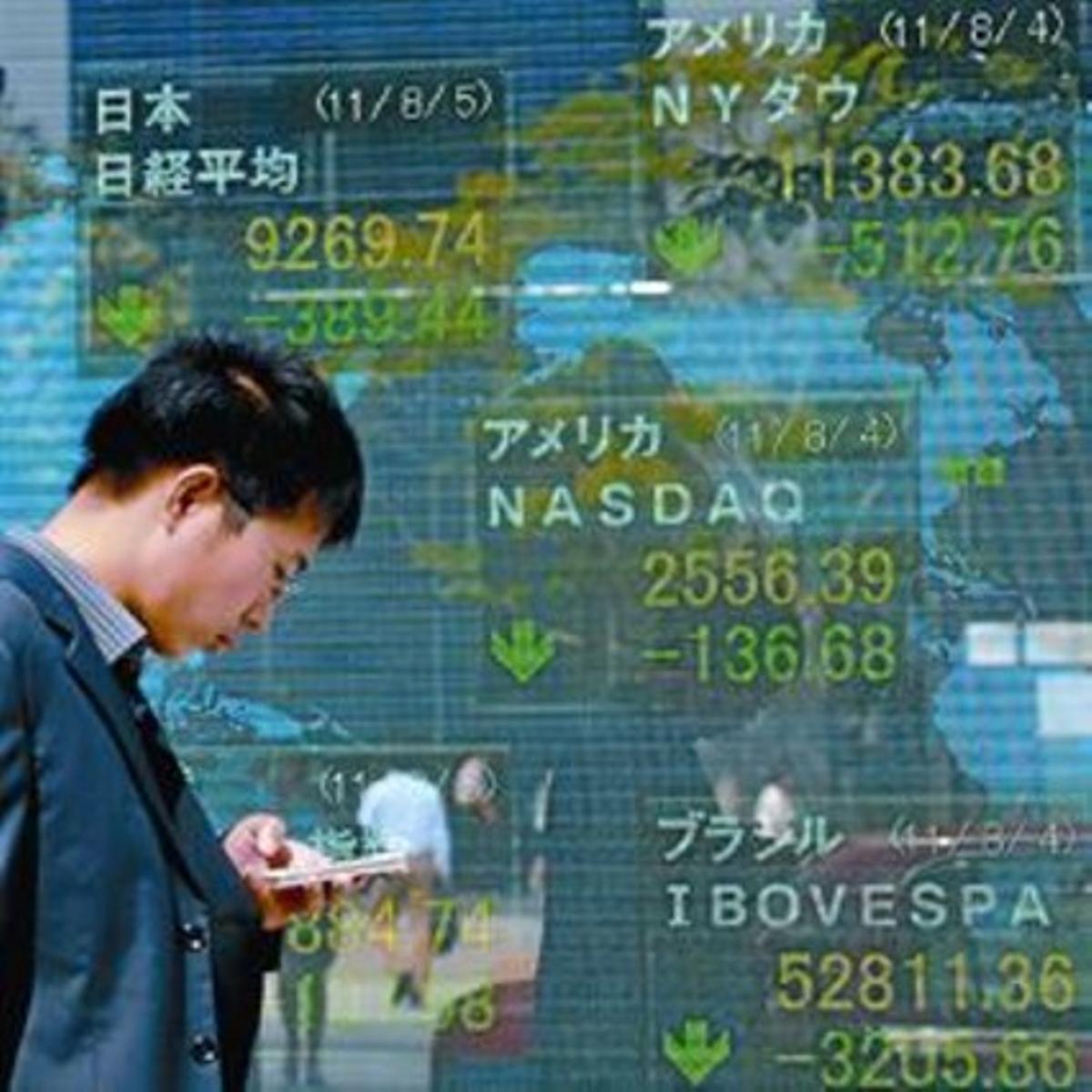 Un hombre consulta su móvil ante un panel informativo en Tokio.