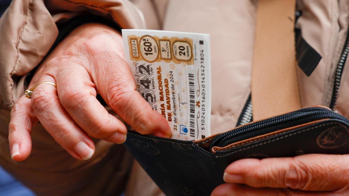 Una mujer mete un décimo de lotería en su monedero.