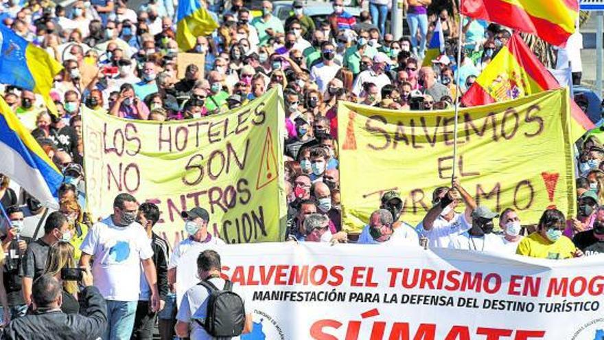 Unos 1.000 vecinos de Mogán se lanzaron a las calles de Puerto Rico, ayer, para manifestarse con el objetivo de recuperar el uso turístico de los hoteles en los que hay 3.200 migrantes. Los pocos turistas de la zona contemplaron la escena sorprendidos y aprovecharon para sacar fotos y animar desde la distancia la iniciativa. | juan carlos castro