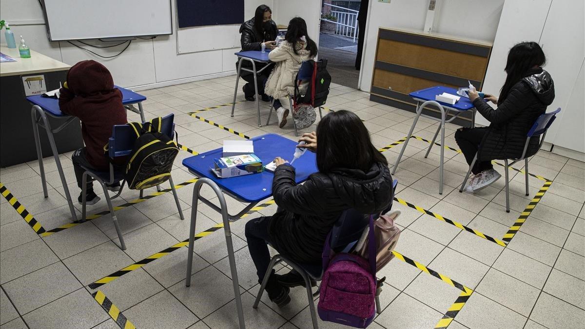 La cinta marca el espacio de cada persona para asegurar el distanciamiento social mientras un maestro ayuda a un estudiante de una escuela pública que ha sido reutilizada como una guardería para menores con padres que trabajan y que viven en el vecindario de Barnechea, Santiago de Chile.