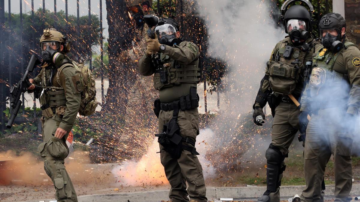 Un aparato detona detrás de agentes de aduana que disparan gas pimienta contra manifestantes, este sábado en Paramount, California.