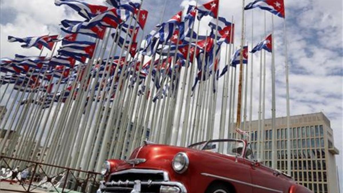 Un coche clásico americano pasa al lado de la embajada estadounidense en La Habana, donde ondean decenas de banderas de Cuba.