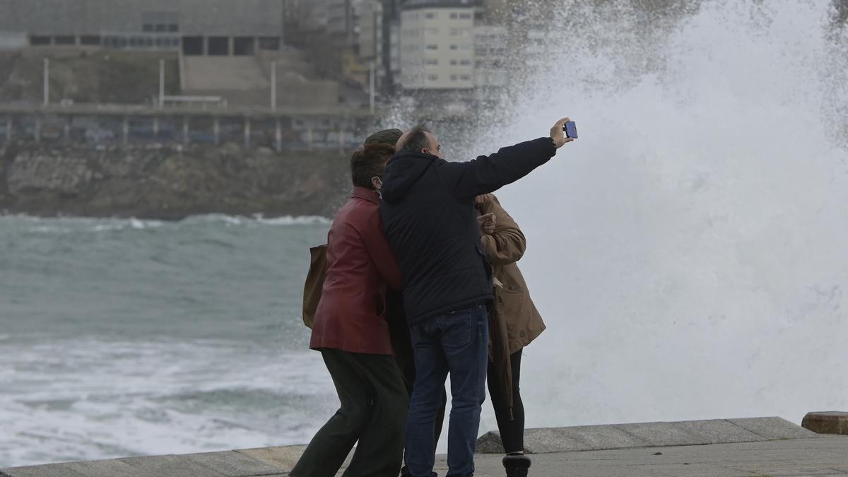 Un grupo de personas se fotografía en la zona de las Esclavas, en A Coruña, con fuerte oleaje al fondo.