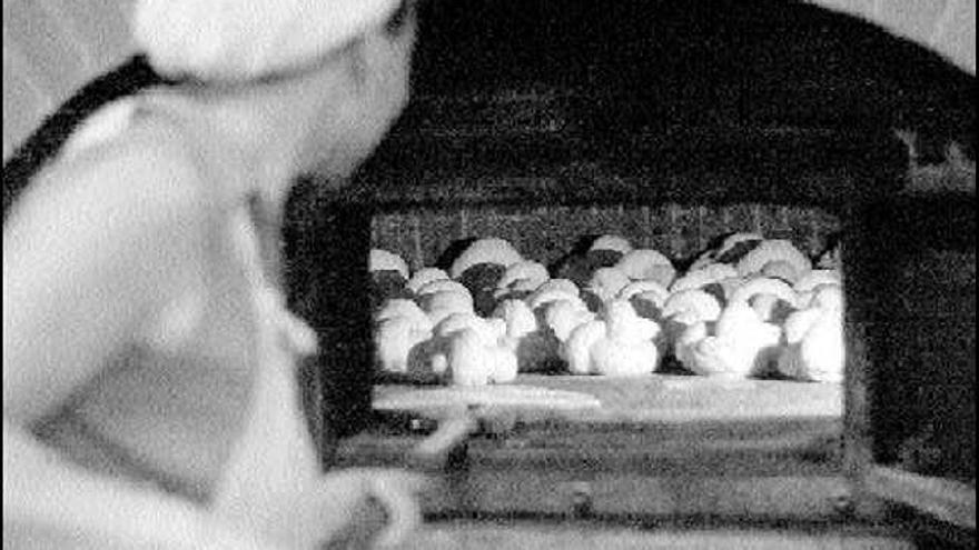 Una panadera introduce unas piezas de pan de escanda en el horno.