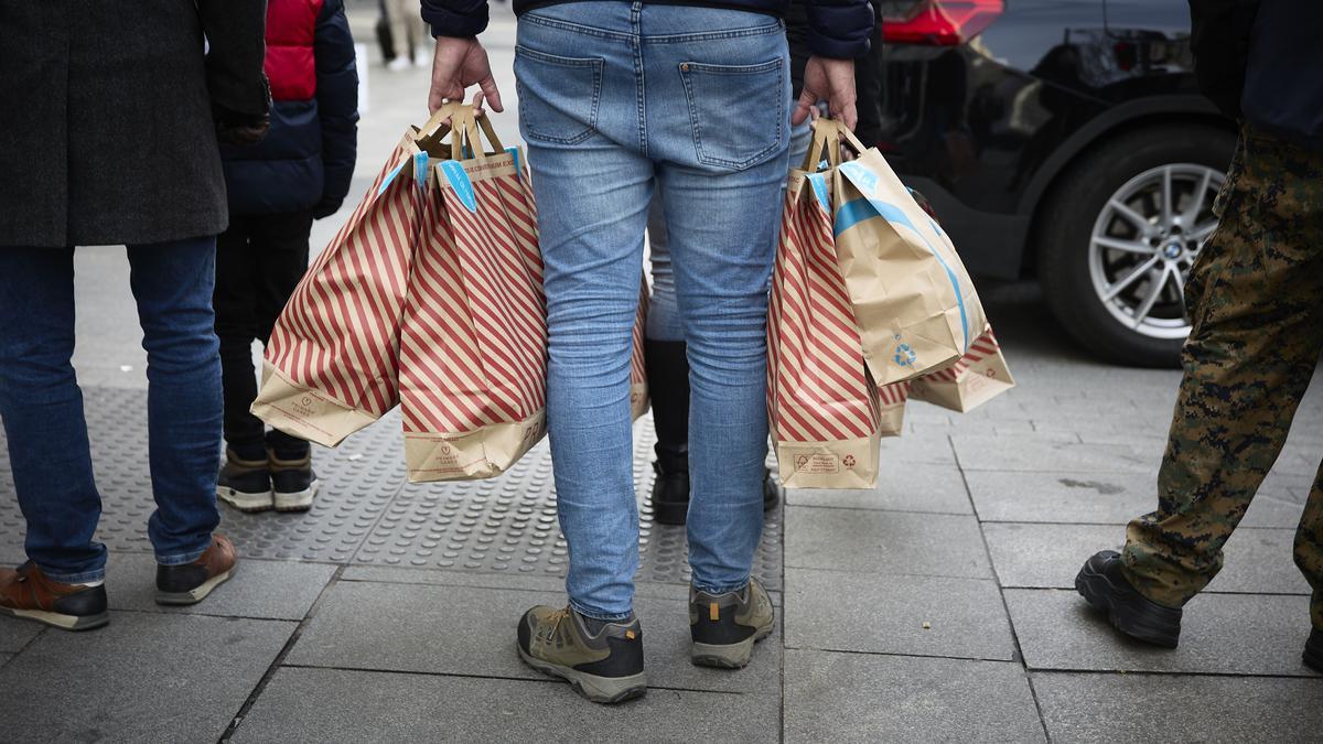 Una persona cargada con bolsas en una calle comercial