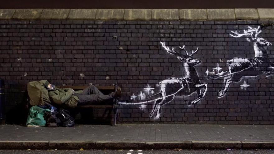 Un hombre yace en un banco junto al mural de Banksy.