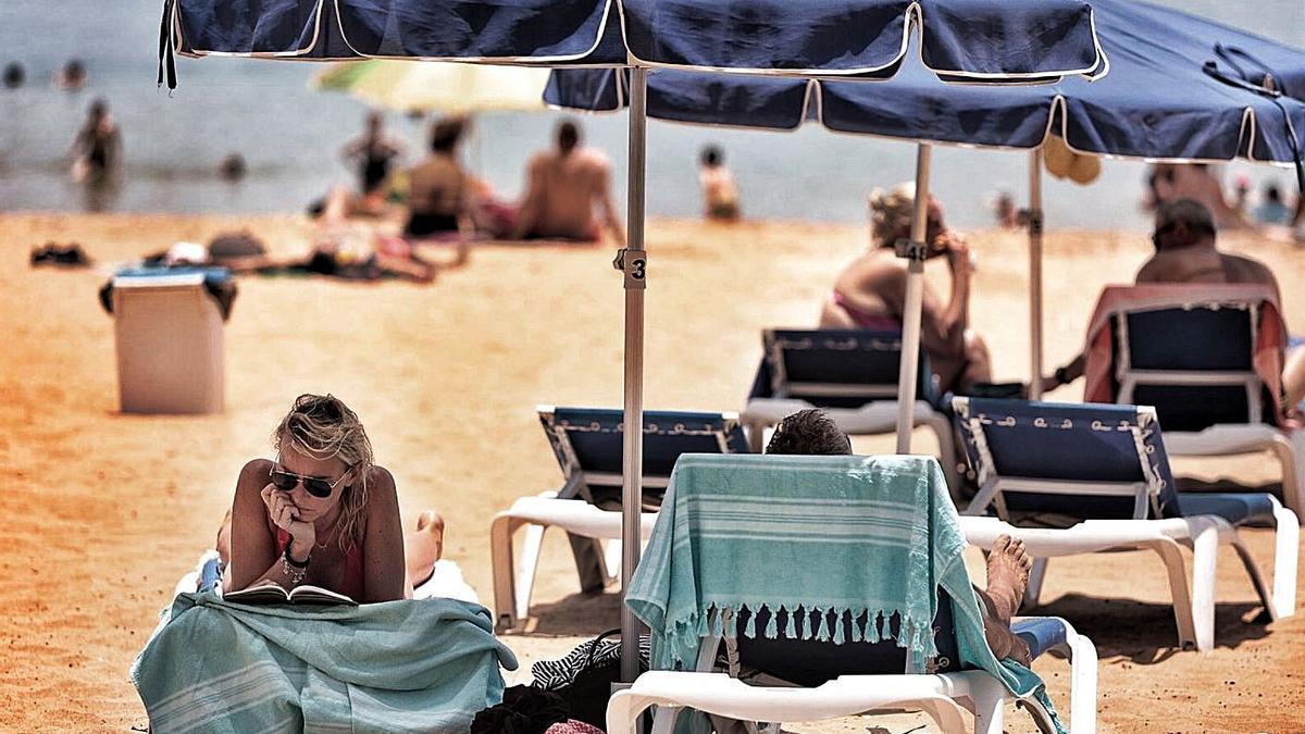 Una usuaria de una playa tinerfeña lee debajo de una sombrilla.