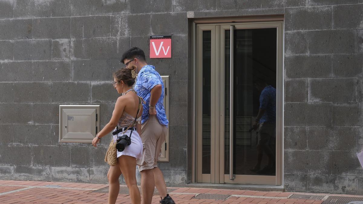 Una pareja pasea por delante de un cartel de una vivienda vacacional.