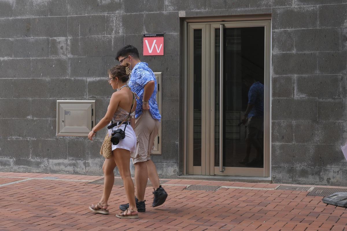 Una pareja pasea por delante de un cartel de una vivienda vacacional.