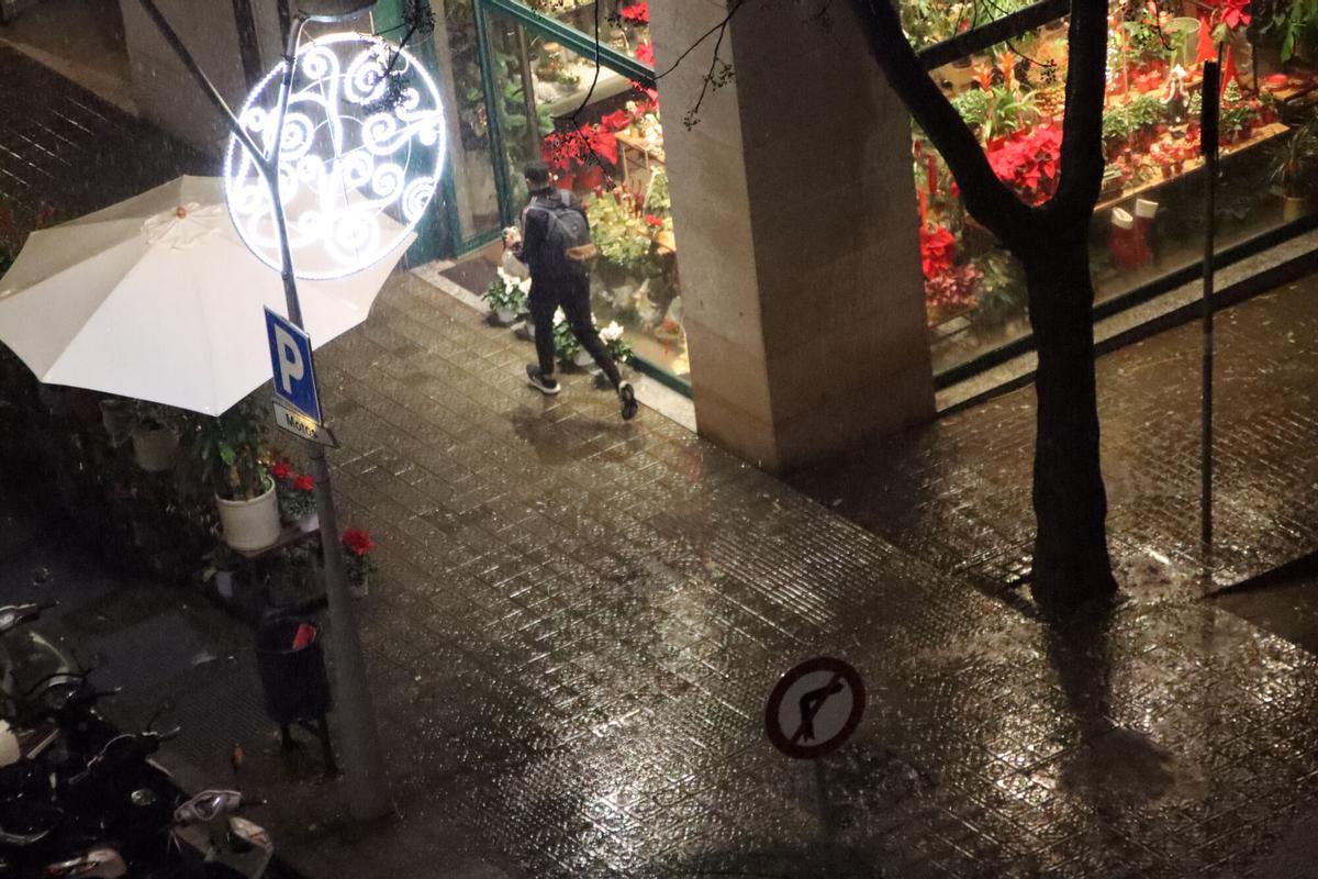 Un chico corre para no mojarse en el Eixample de Barcelona