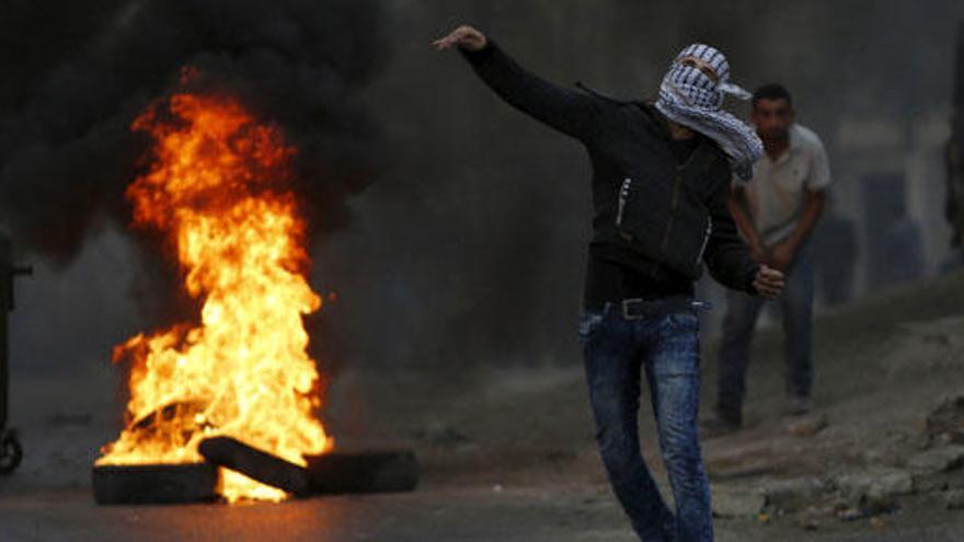 Un palestino lanza una piedra contra soldados israelíes.