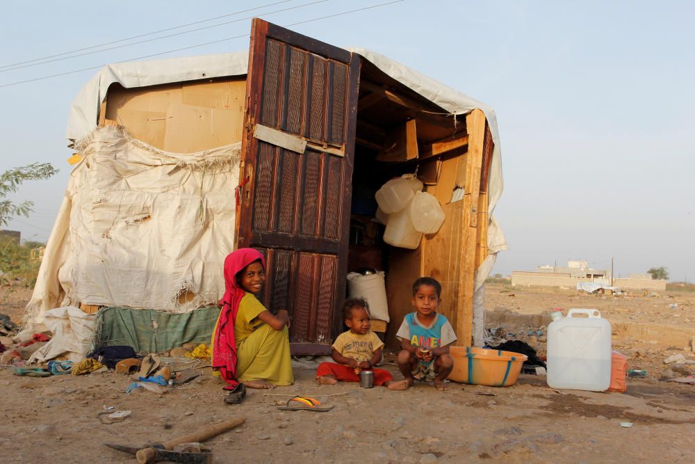 Children sit next to their hut at a makeshift ...