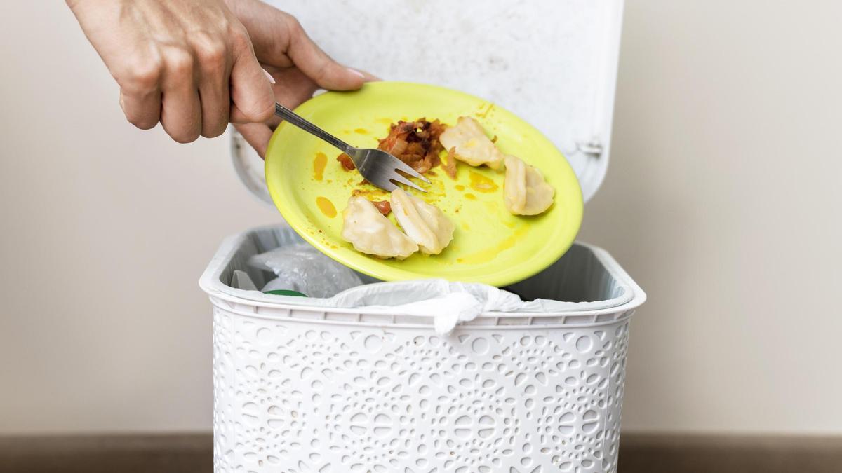 Una persona tira restos de comida en el cubo de la basura