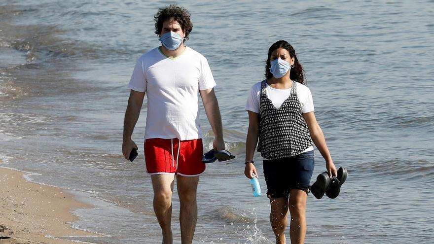 Dos personas con mascarilla caminan por la orilla de la playa de la Malvarrosa de Valencia.