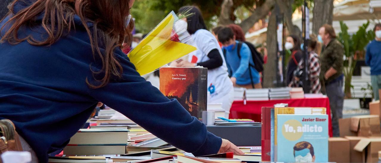 Una noia remena, amb una rosa a la mà, llibres a la parada de la Llibreria Hipérbole a Vara de Rey.