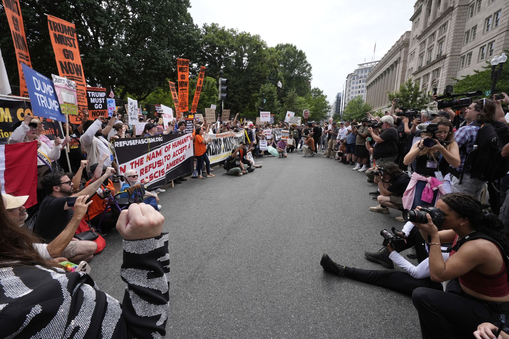 Demonstrators stand near the White House, left, as people and members of the media document during a protest taking place on the day of a military parade commemorating the Army's 250th anniversary, coinciding with President Donald Trump's 79th birthday, Saturday, June 14, 2025, in Washington. (AP Photo/Alex Brandon)