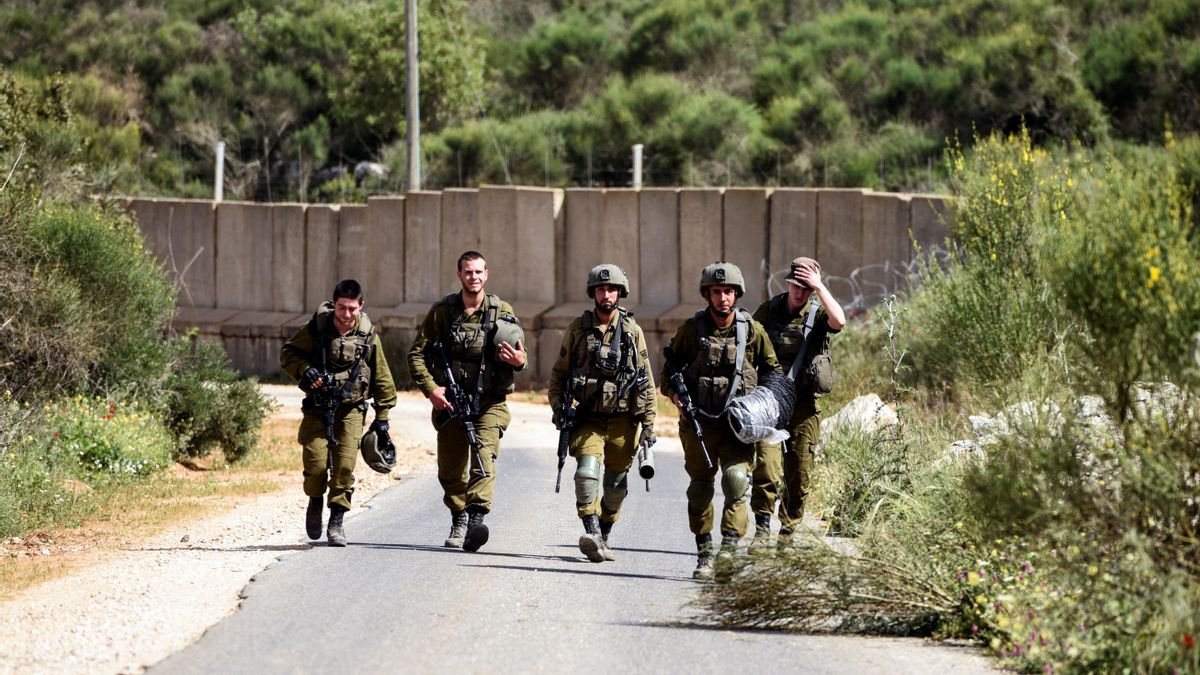 Israeli soldiers walk next to the Israel-Lebanon border near Shtula