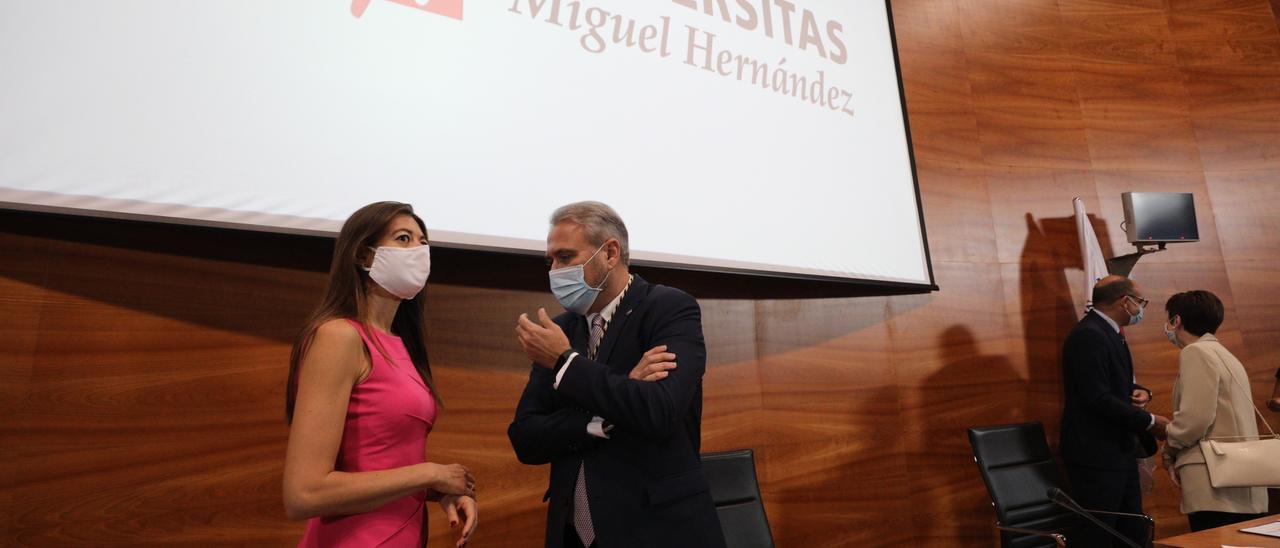 El rector y la consellera de Universidades, en un acto en el rectorado, tras ellos el logo de la UMH