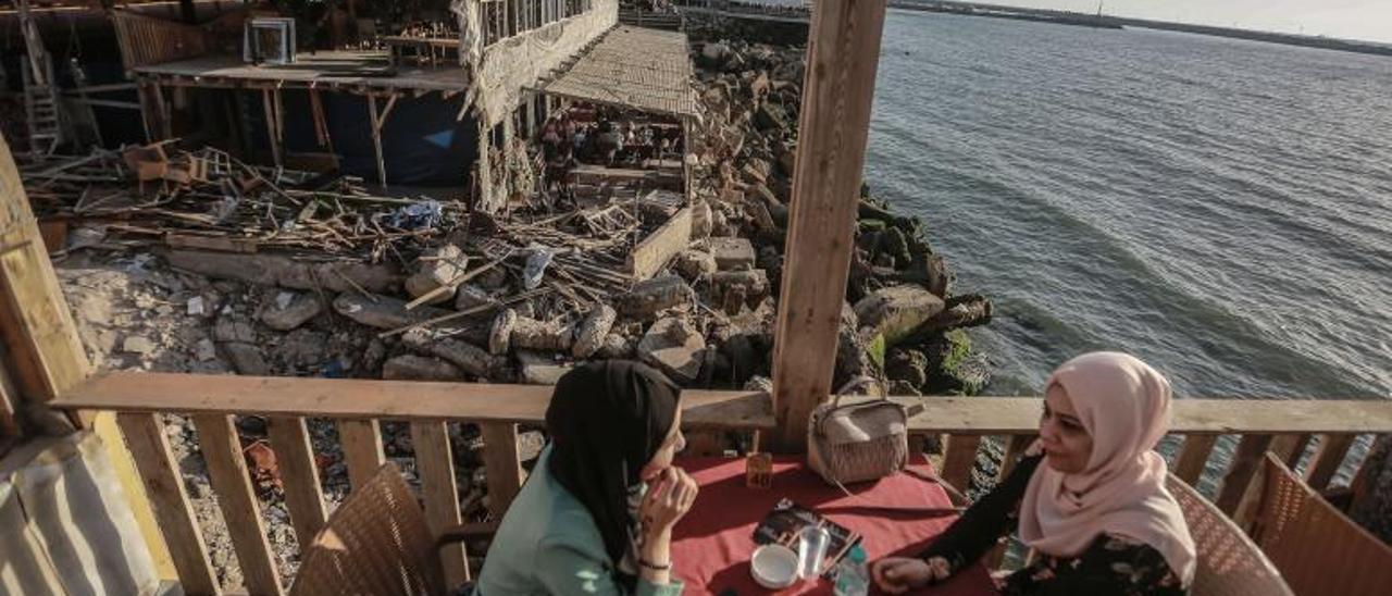 Dos mujeres palestinas en la terraza de un restaurante de Gaza ubicado justo al lado de un inmueble destruido por misiles israelíes. | | DPA-EUROPA PRESS