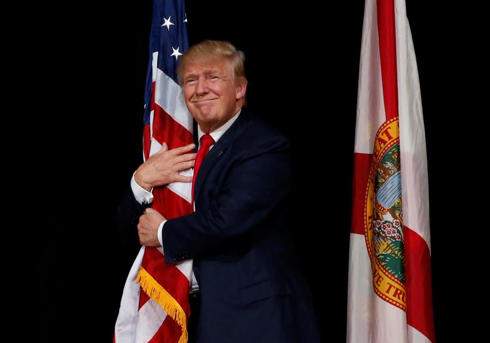 Trump hugs a U.S. flag as he comes onstage to ...