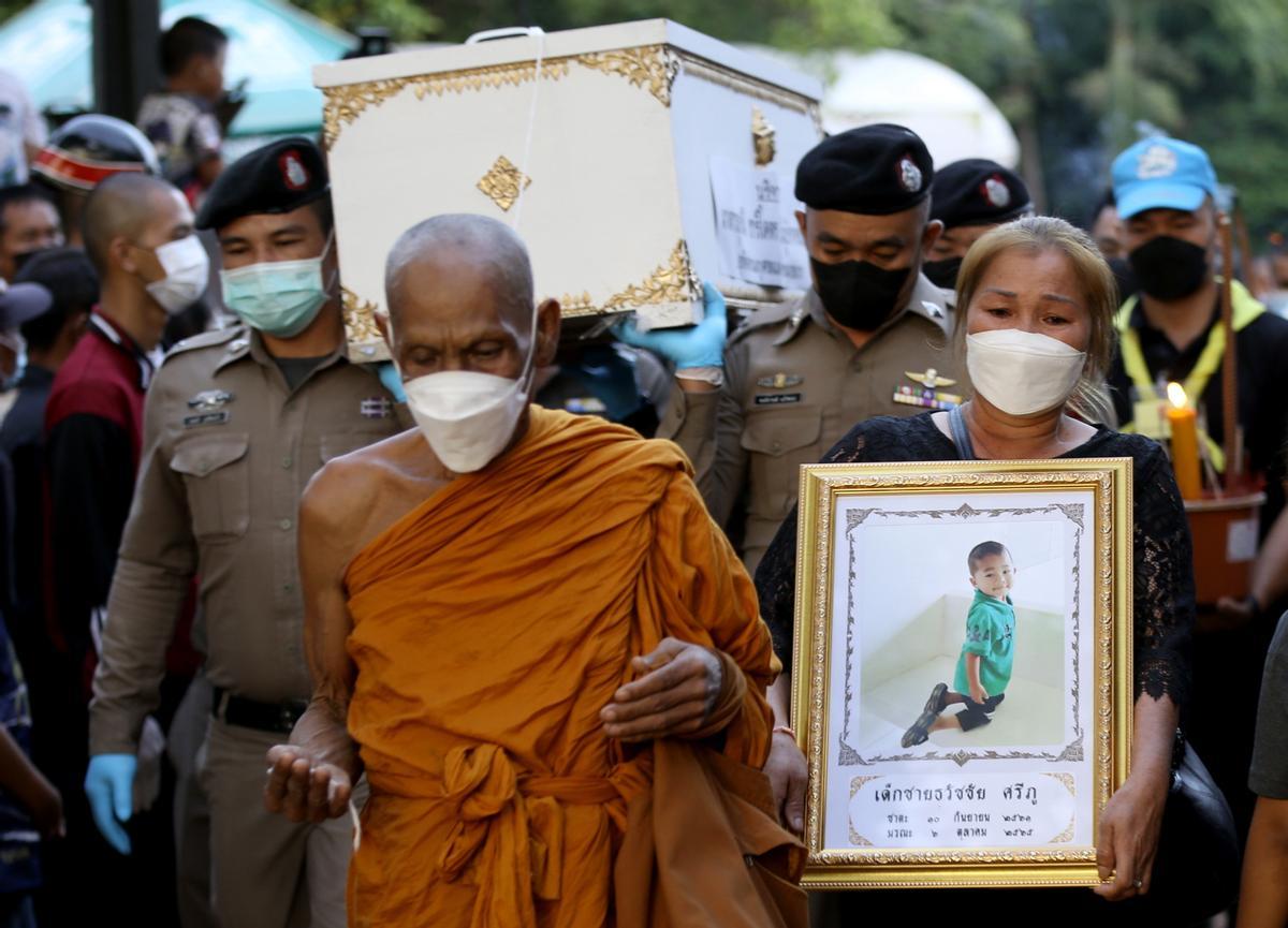 Un monje budista tailandés conduce a una madre de luto con el ataúd de su hijo a la pira funeraria durante la cremación masiva patrocinada por la realeza