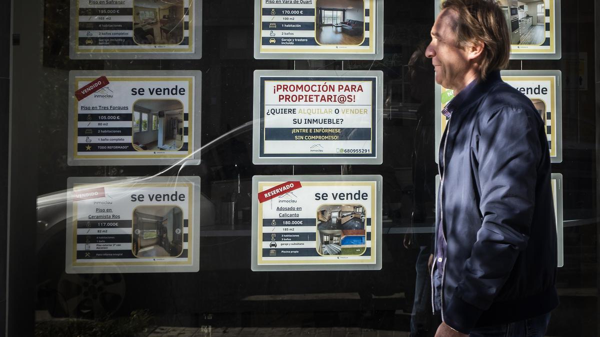 Un hombre pasa ante el escaparate de una inmobiliaria con pisos vendidos.
