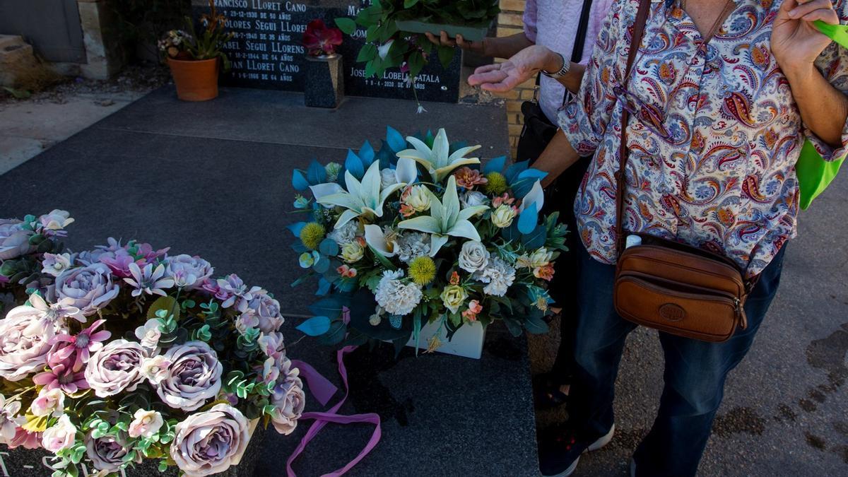 Una mujer porta flores de tela en el Cementerio de Alicante.