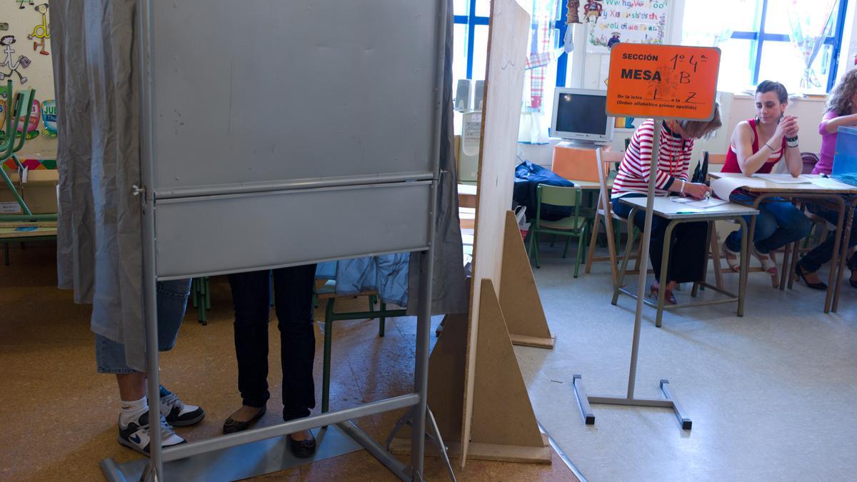 Dos personas seleccionan las papeletas para votar en un colegio electoral