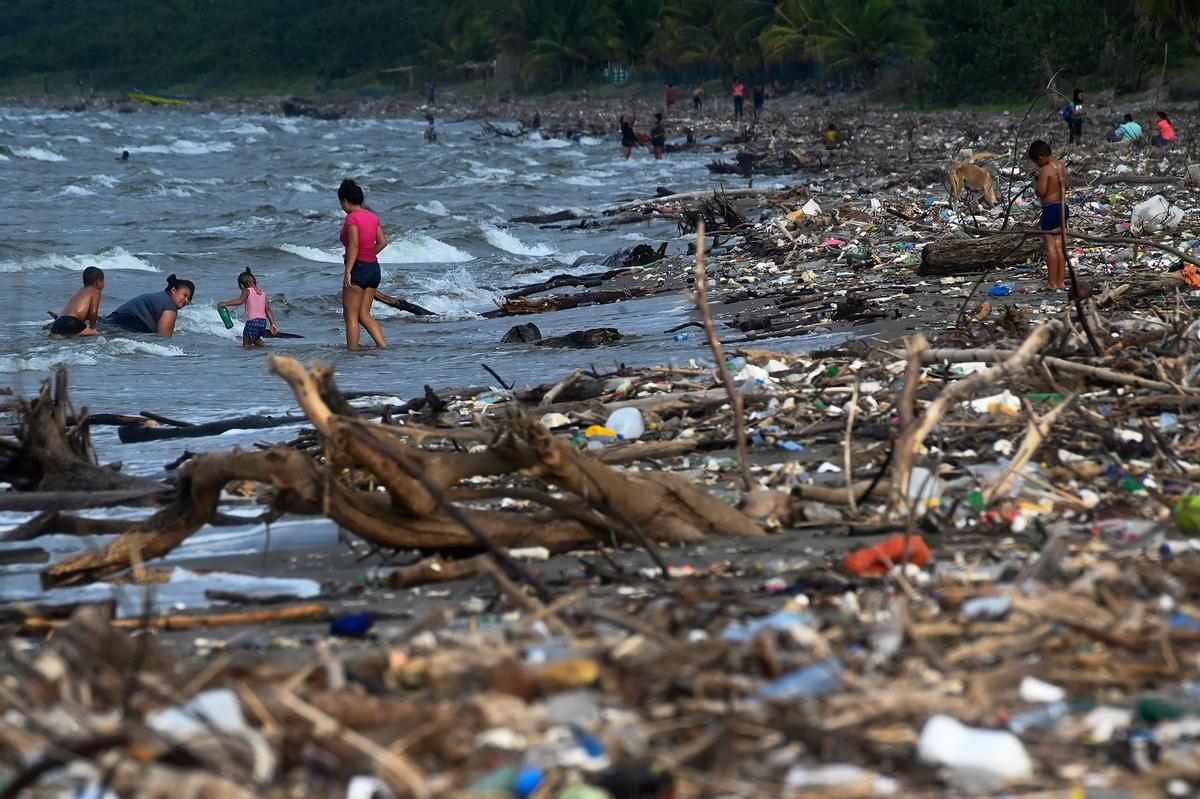 Una familia se baña en una playa llena de residuos, plásticos y otros deshechos en Omoa, Honduras, el 10 de septiembre del 2022.