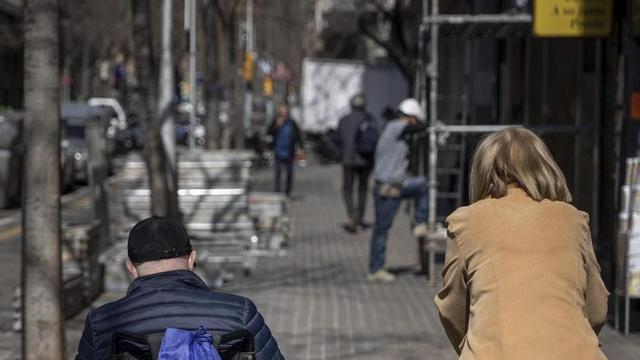 Un home en cadira de rodes passeja al costat d’una dona. | FERRAN NADEU