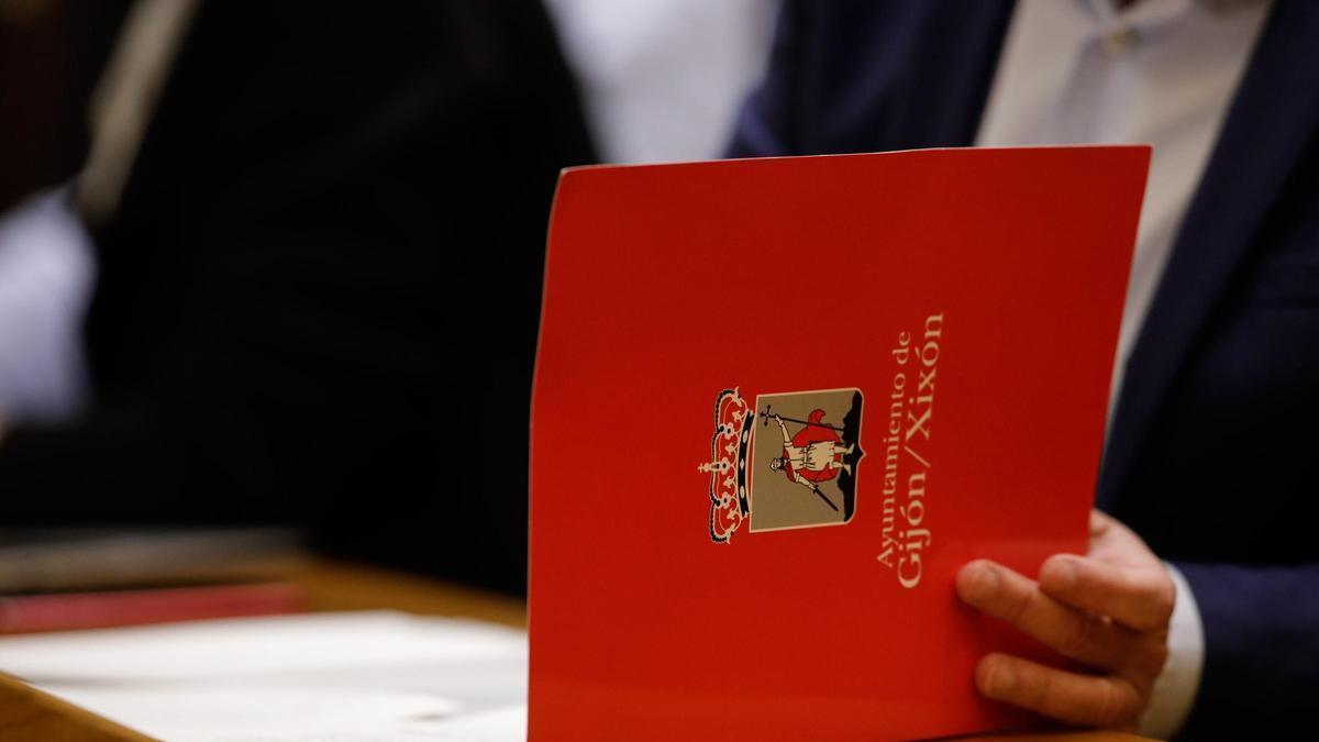 Una persona mira documentación en una carpeta con el escudo del Ayuntamiento de Gijón.