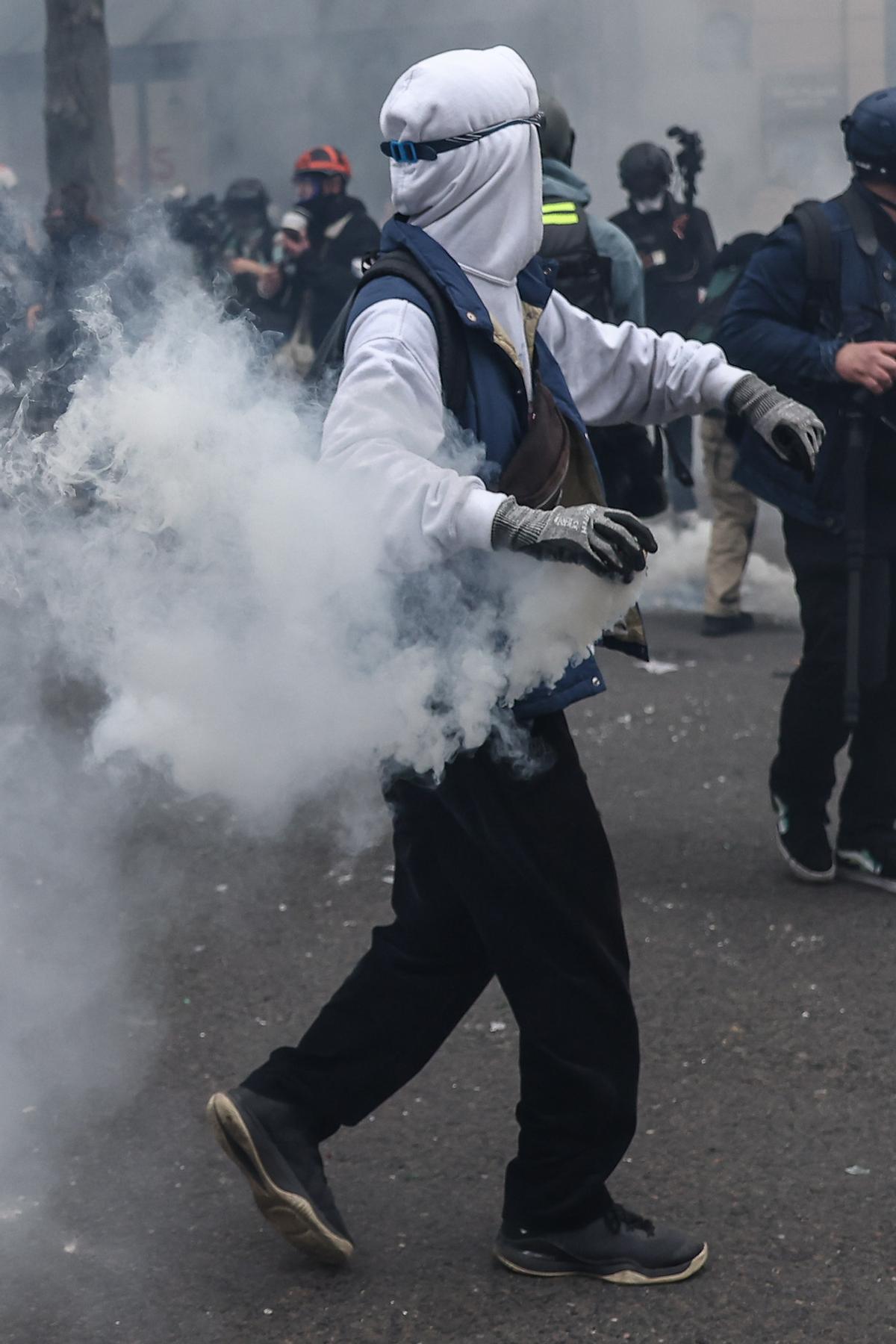 Paris (France), 23/03/2023.- A protester throws a tear gas during clashes with anti-riot police during a demonstration against the government pension reform in Paris, France, 23 March 2023. Protests continue in France after the French prime minister announced on 16 March 2023 the use of Article 49 paragraph 3 (49.3) of the French Constitution to have the text on the controversial pension reform law be definitively adopted without a vote in the National Assembly (lower house of parliament). The bill would raise the retirement age in France from 62 to 64 by 2030. (Protestas, Francia) EFE/EPA/MOHAMMED BADRA