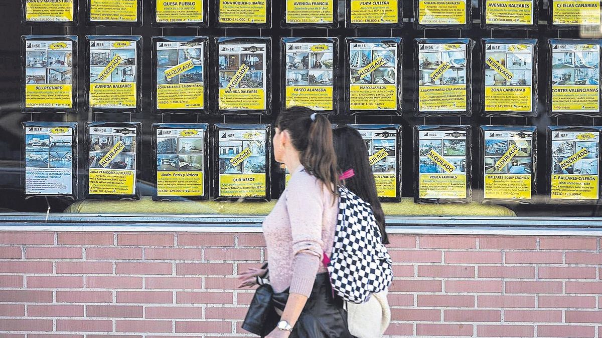 Dos mujeres pasan por delante de una inmobiliaria con carteles de alquilado o vendido.