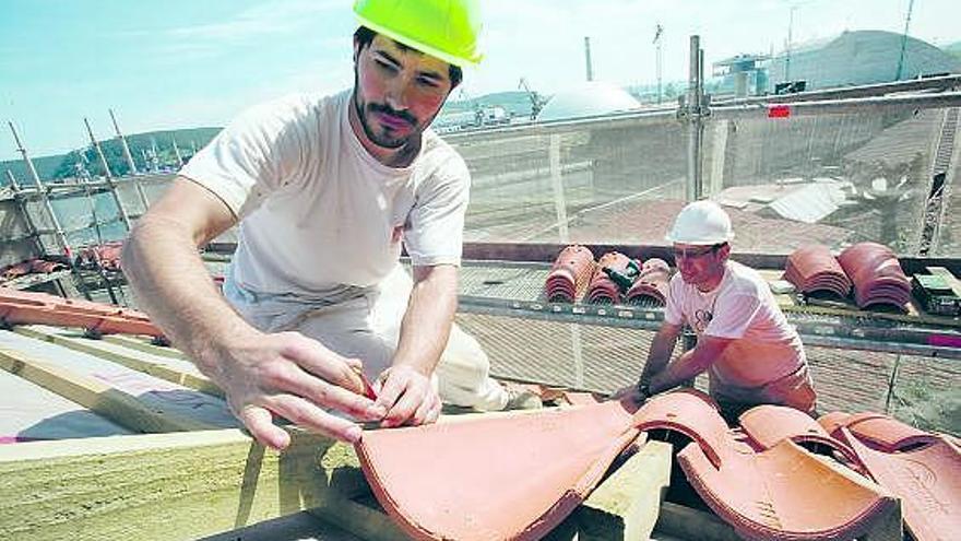 Dos obreros colocan las tejas de la nueva cubierta de la capilla, con la cúpula del Niemeyer al fondo.