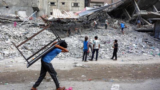 Un nen carrega una taula a l’esquena davant la runa d’un edifici destruït per Israel a Gaza, diumenge. | OMAR AL-QATTAA / AFP