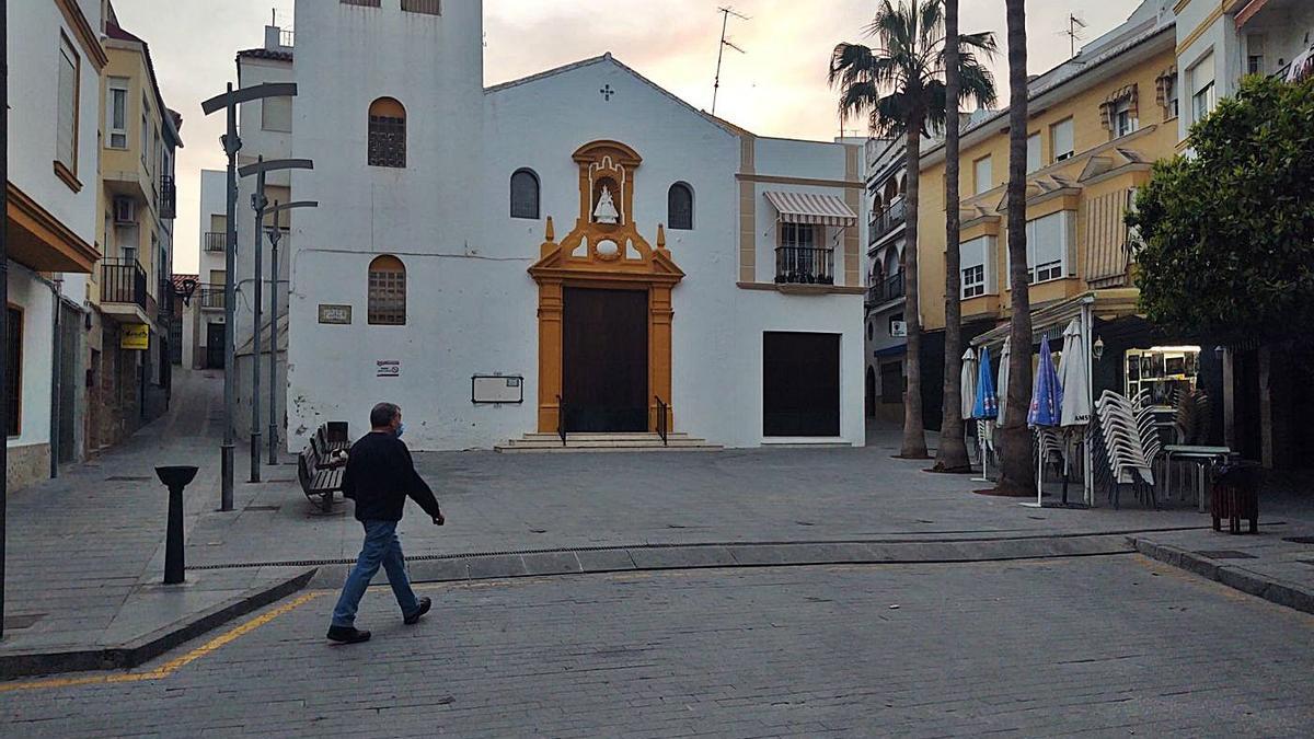 Doña Mencía | Un vecino pasa delante de la iglesia del Espíritu Santo, con las sillas del bar de al lado plegadas. | F, FLORES / CASAVI