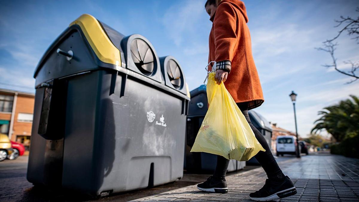 Una mujer recicla envases de plástico en el contenedor amarillo